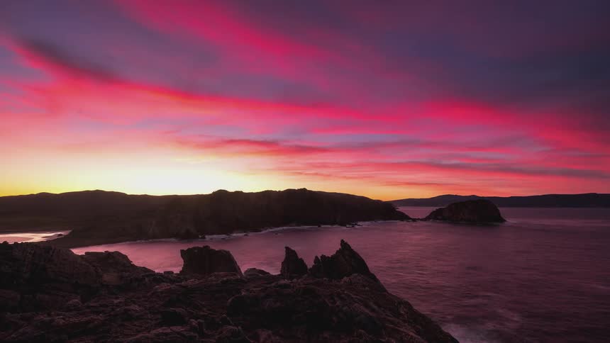 Time lapse of a sky with hues of blue and yellow during a sunrise over the coast