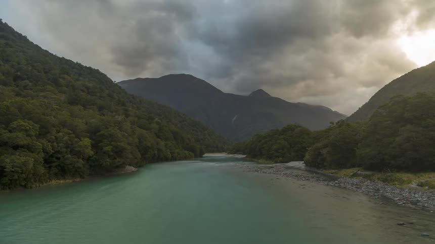 Greenish river surrounded by mountains and forests on a cloudy day