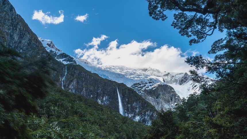 Time lapse of a waterfall in the mountains under a blue sky with rolling clouds