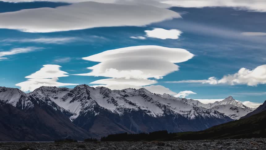 Clouds expand and form mushroom shapes over a snow dappled mountain range