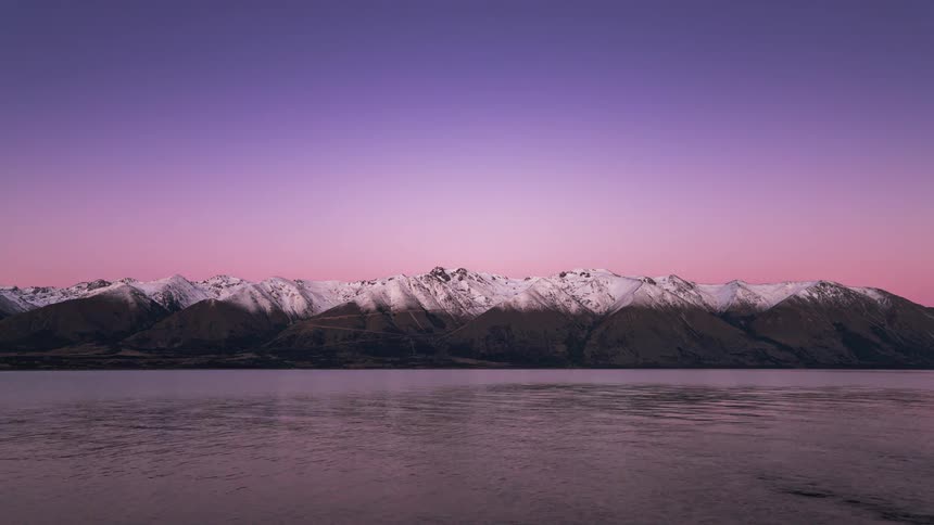 Lake surrounded by mountains with snowcapped peaks and dusk