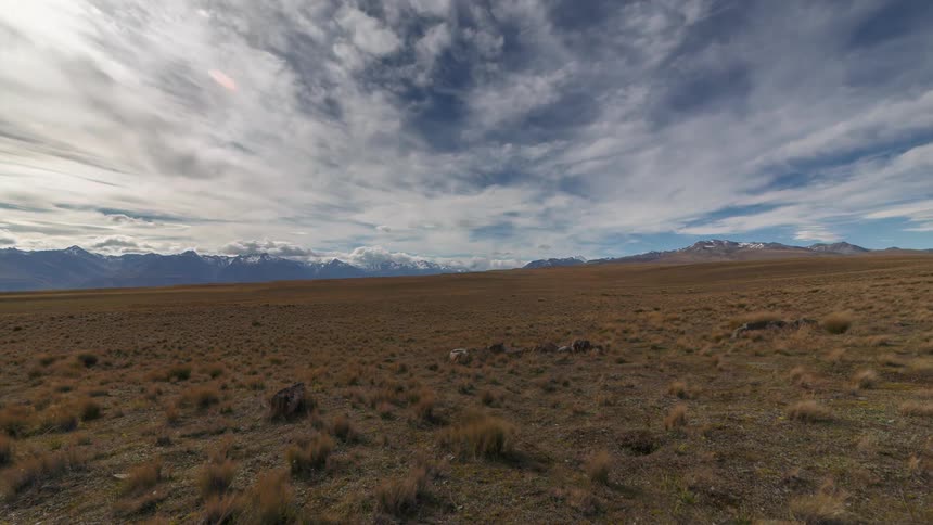 Dry field with mountains on the horizon and clouds passing by