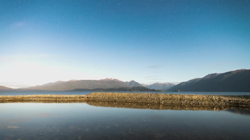 Landscape of a lake that reflects the silhouettes of mountains on the horizon and the dawning day