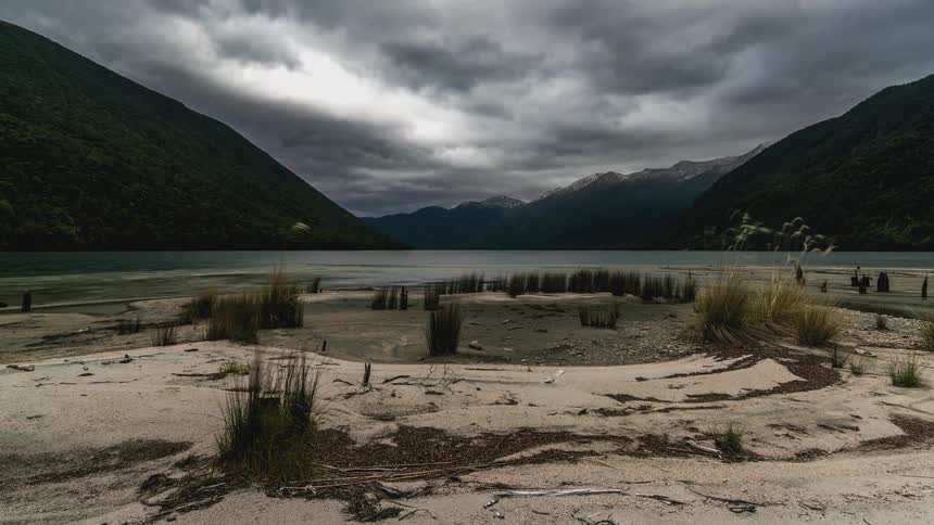 Lake surrounded by mountains and dense vegetation under a cloudy sky