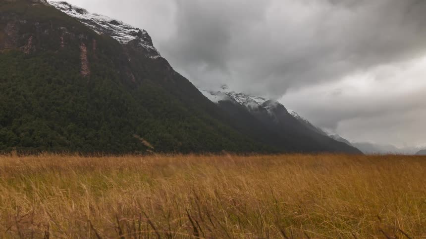 Countryside surrounded by mountains with snowcapped peaks on a cloudy day