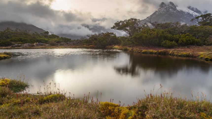 Timelapse of a placid lake surrounded by dense vegetation near the mountains