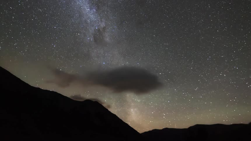 A starry sky with part of a nebula visible and clouds passing across the sky