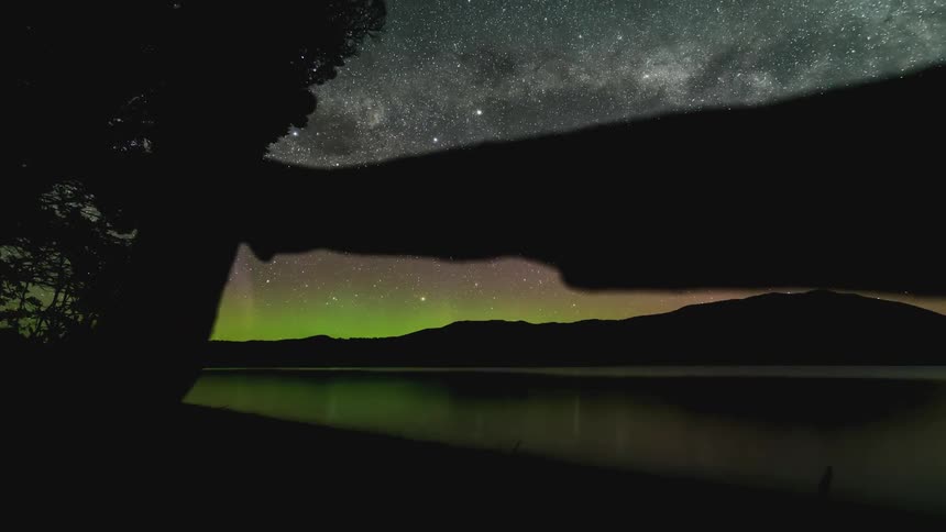 Time lapse of green auroras and a starry night sky over a lake in the mountains