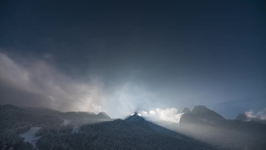 Sun flares as it passes behind a forested mountain in the winter