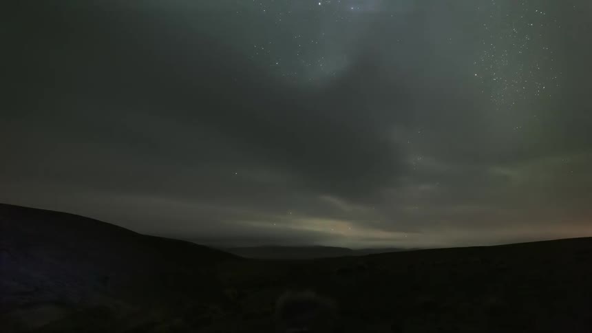 Time lapse of a starry night sky covered by clouds on over a dark landscape