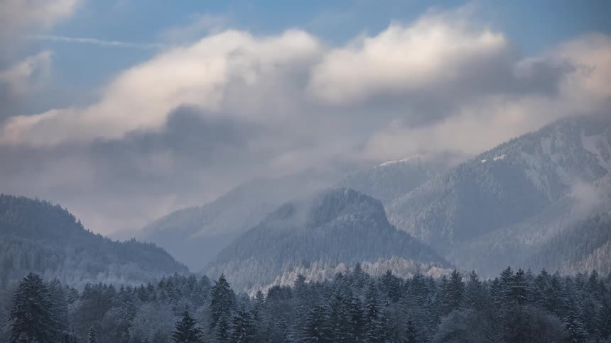 Time lapse of layer of clouds rolling over the slopes of a mountain range
