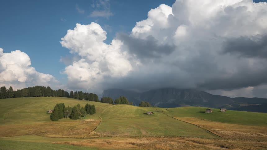 Time lapse of clouds rolling over a rural landscape next to the mountains