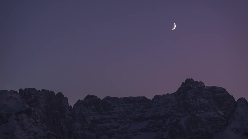 Mountainous landscape with snow and the moving moon in a sunrise