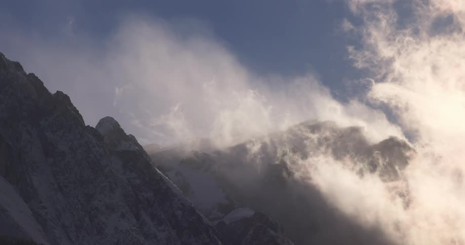 Clouds hang over the snow covered slopes of a mountain range