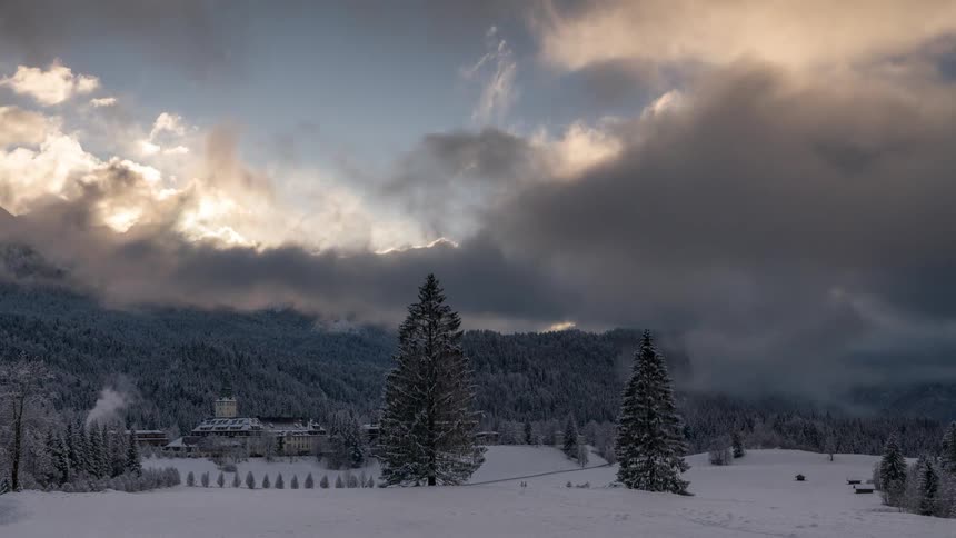 Houses on a snowcovered mountain with forests around and clouds passing by