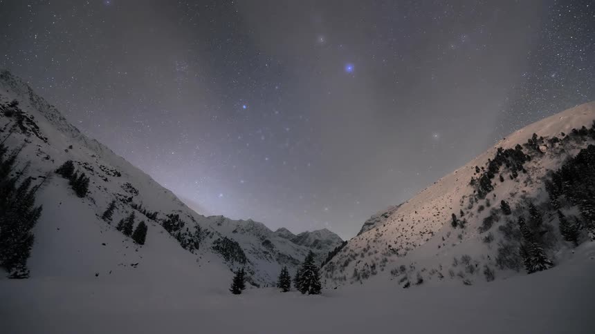 Time lapse of a starry sky and a sunrise over a snowy mountainous landscape