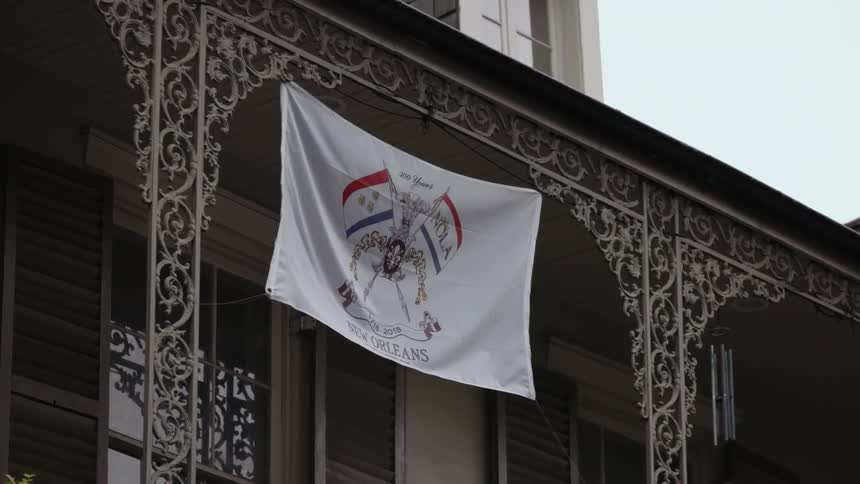 A new orleans banner hangs from an ornate porch railing