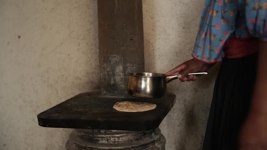 A person is cooking flat bread with a pot and stove