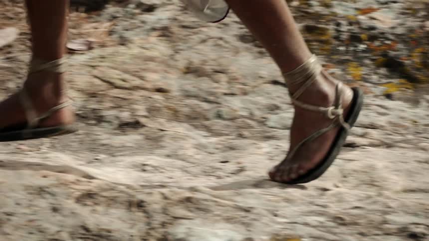 A person wearing sandals is running on a rocky path