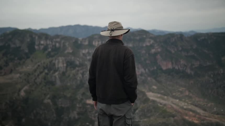 A man stands and looks out over the hills and valley below