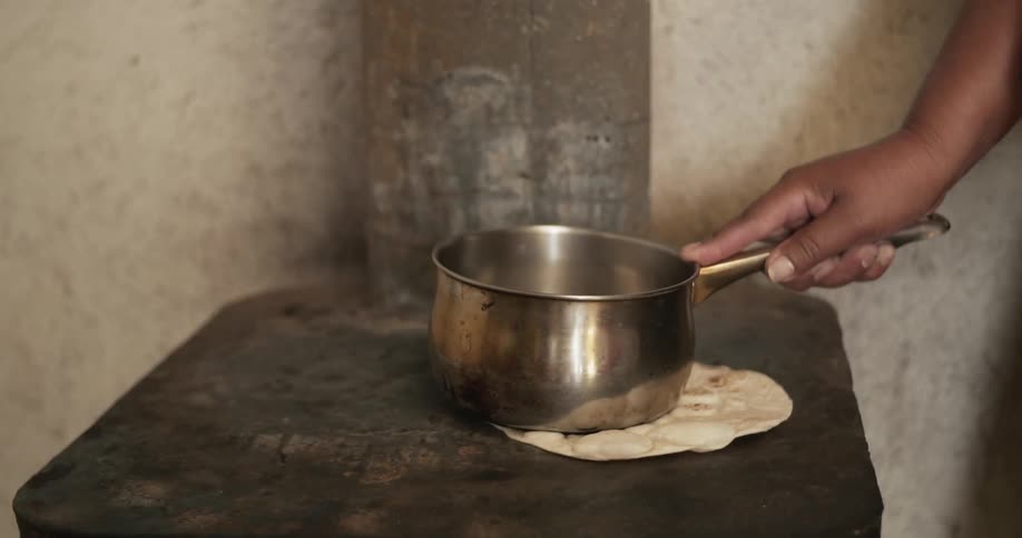 Person using a pot to flatten and cook tortilla on hot stove