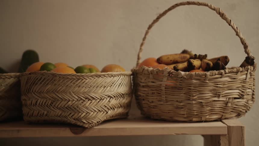 Several straw baskets of fruit sitting on a shelf