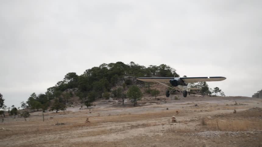 A propeller plane takes off from a dirt runway