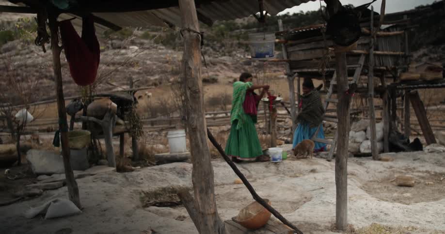 An indigenous woman is turning a crank on a pump as another stands by her