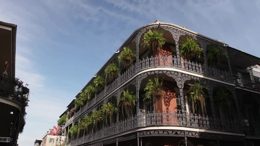 Looking up at a building on the corner of a street with green hanging plants all along the sides