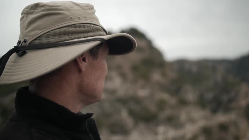 Close up of a man wearing a hat looking towards a barren hillside