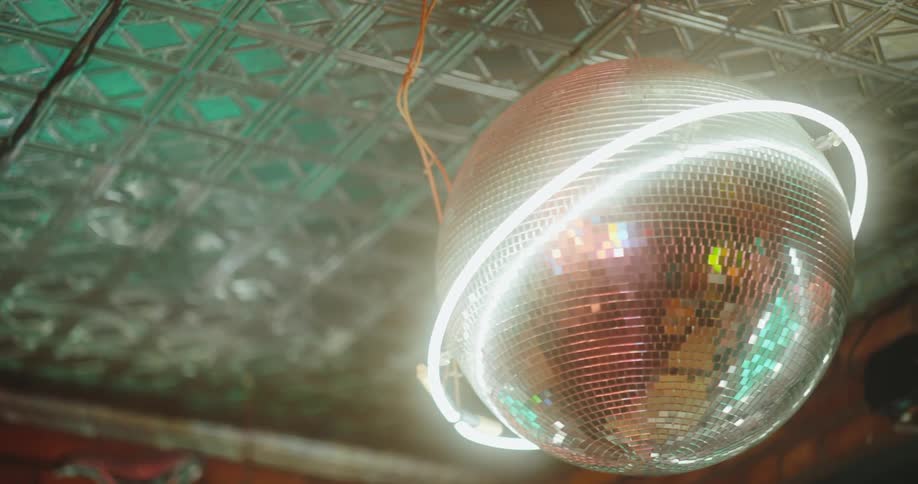 A disco ball with neon tubes wrapped around it hanging from a ceiling