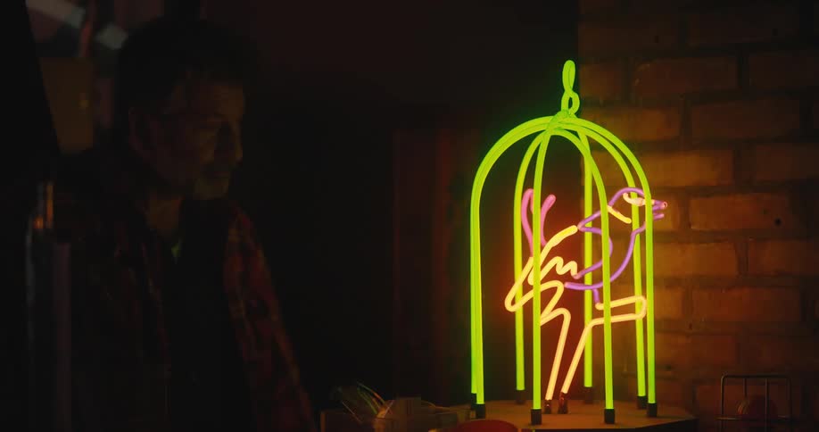 A man turning on a bird cage shaped glowing neon sign in the dark environment