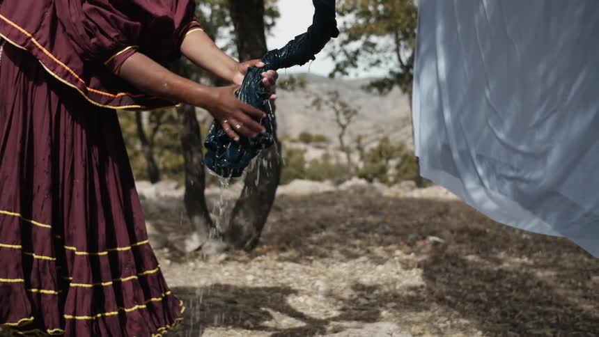 Woman wringing water from him clothes that she has hanging on a line