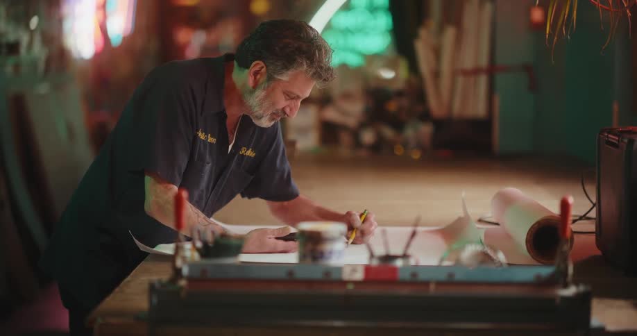 A gray-haired artisan drawing a design blueprint in his workshop
