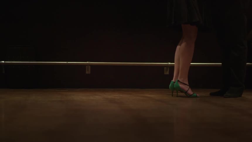 The legs of a woman in green heels walking on a bright wooden floor