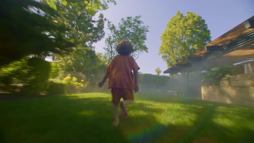 A young boy runs through the grass in the backyard of a house