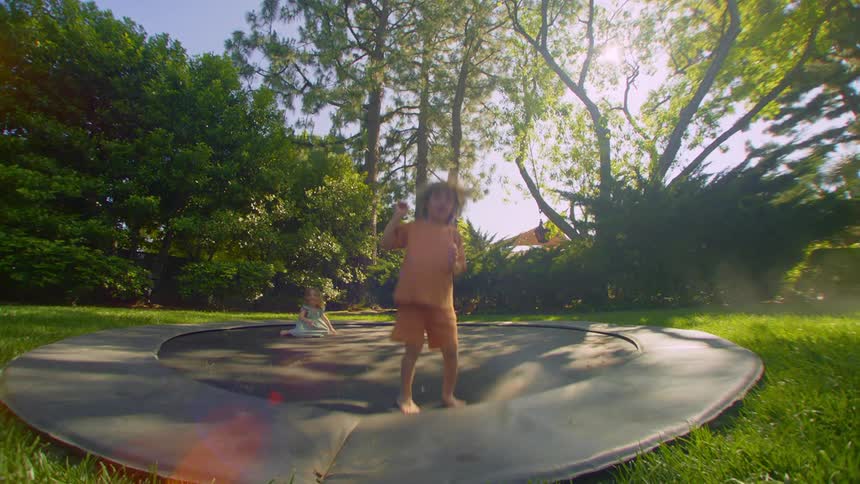 Two kids jump on a ground trampoline in a yard