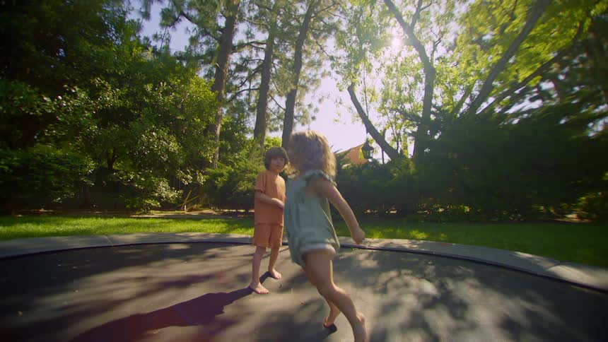 Kids play on large trampoline in the backyard on a sunny summer day