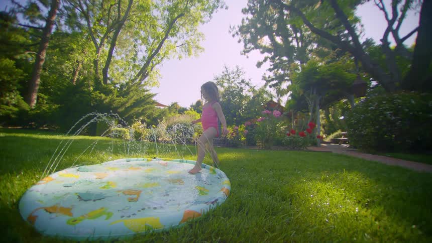 A little girl in a pink bathing suit laughs while stepping into a water pool