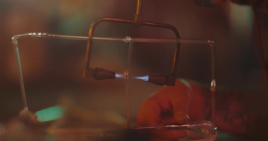 A person holding a double-ended blowtorch to melt a transparent pipe