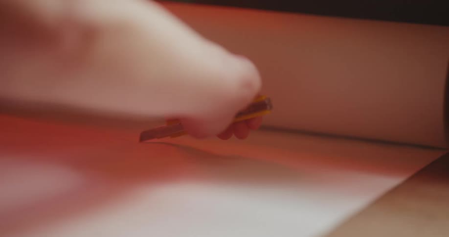 A human hand cutting orange paper using a pointed utensil