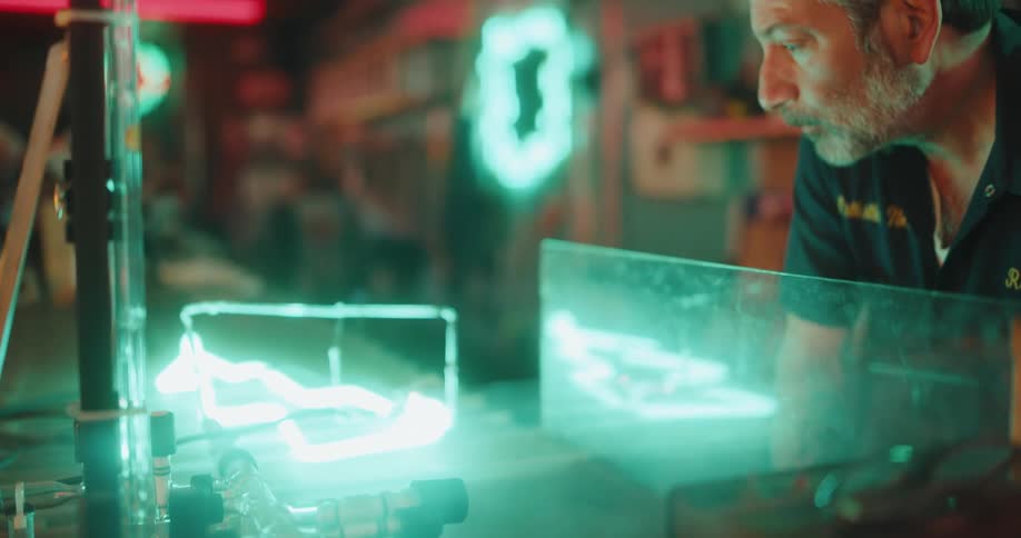 A man in a workshop turns the dial on to test a neon light
