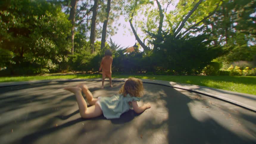 Two young siblings bounce on a trampoline outdoors during midday