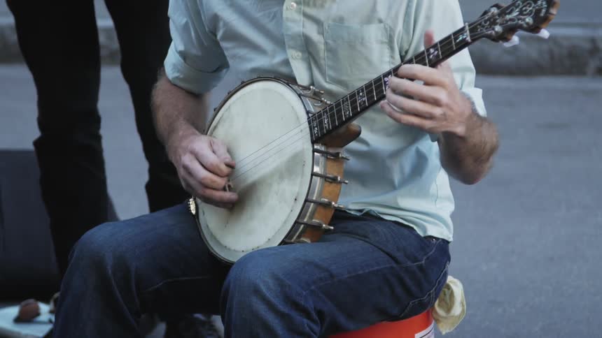 A man plays a banjo while another person taps their foot