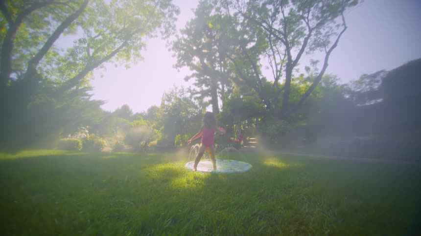 A little girl is playing in a small pool in a grassy backyard and she jumps out of the pool