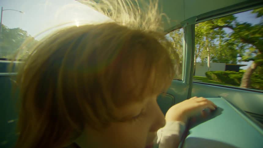 A little boy is standing on a seat of a car looking at the journey from behind and then looks ahead