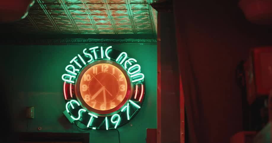 A neon sign with white writing and an orange clock in the center