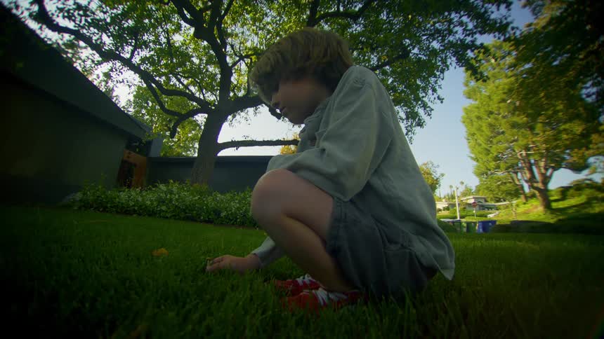 Little boy crouched in the grass burying a leaf in a yard