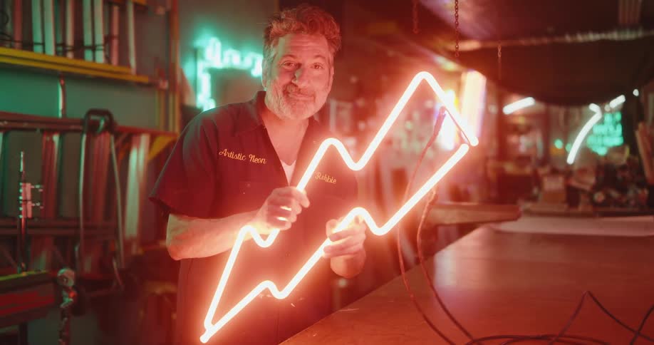 Man holding a sign in the shape of a lightning bolt with red neon light