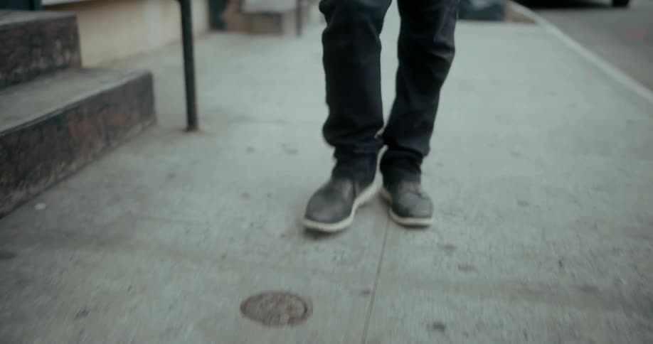A man is shown from knees to feet walking slowly on a sidewalk